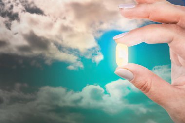 Kadın parmaklarını mavi gökyüzüne karşı antidepresan kapsülü tutuyor. Depresyondan çık.