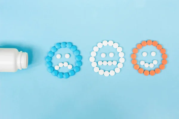 Pillole multicolori e facce divertenti e una bottiglia di plastica su sfondo blu. Il concetto di antidepressivi e guarigione. Copia spazio . — Foto Stock