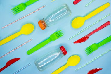 Açık mavi arka plan üzerinde çatal, bıçak, kaşık, pipet, şişe gibi renkli tek kullanımlık sofra bir sürü. Plastik ücretsiz konsept.