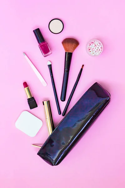 Макияж продуктов разлива из черного лакированного косметического пакета на пастельно-розовом фоне — стоковое фото