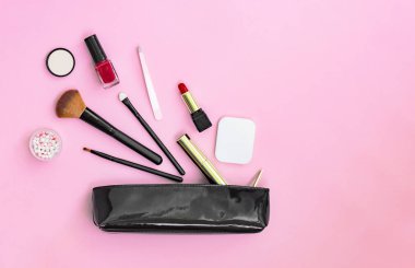 Pastel pembe arka plan üzerine siyah vernikli kozmetik torbasından dökülen ürünleri makyaj