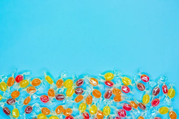 Bright multicolored candies in wrappers of transparent mica, sweets on blue background, colorful candy scattered, top view with copy space