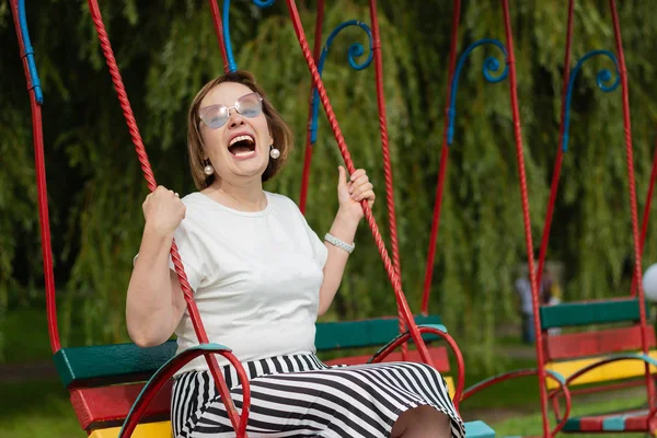 Riendo mujer madura en un columpio en un parque infantil — Foto de Stock