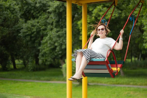 Mujer madura mayor disfrutando de la vida de jubilación sintiéndose feliz y saludable divirtiéndose balanceándose en un columpio en el parque en un hermoso día soleado . Fotos De Stock