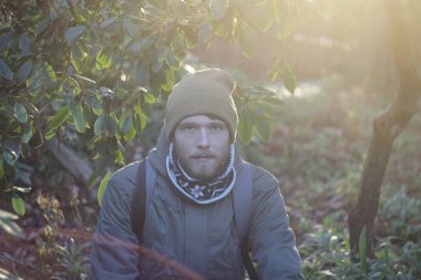 Genç sarışın beyaz adam sakallı bir atkı, şapka ve ormanda yürüyüş sırt çantası