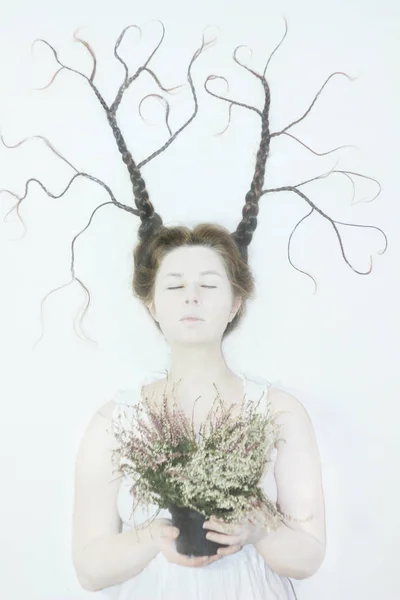 Mom and daughter in white dresses on a white background depict winter and spring, holding flowers and a twig with leaves. Hair braided in braids. Mom braid is in the form of wood