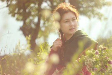 Mutlu bir genç beyaz uzun kızıl saçlı beyaz kadın bir alan üzerinde onun elinde bir buket çiçek ile gülümseyen tam çiçek ve güneş ışığı. Parlak bahar