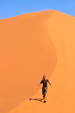 Spor giyim erkek bir gezgin bir Dune Soussefly Milli Parkı, Namibia turuncu kum üzerinde çalışır.