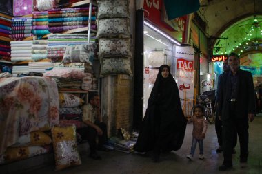 : Qom, Iran - 10 Mayıs 2017: Ünlü İran pazarı (bazaar) ve siyah bir chodor bir tekstil kadının kocasını ve oğlunu sokakta yürürken bir kadın.