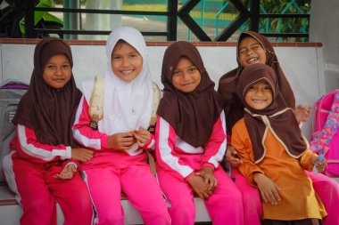 Banda Aceh, Endonezya - 20 Ocak 2018: Türbanlı küçük Endonezyalı çocuklar otobüs durağında okul otobüslerini bekliyor.