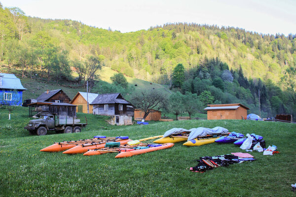 Carpathians, Ukraine - May 8, 2015: Camp of water alloys and kayaks drying on the grass in the Carpathian village on the background of mountains