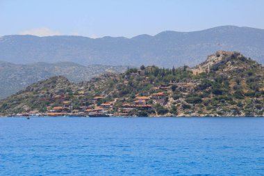 Bodrum bölgesinde küçük bir sahil kasabası, Türkiye'de Akdeniz'de kaya ve dağların arka planına karşı. Türk bayraklı kale.