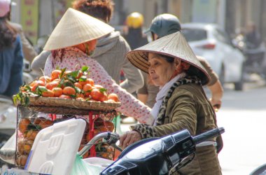 Hanoi, Vietnam - 23 Şubat 2016: Vietnamlı sokak satıcıları (turunçgil meyveleri, mandalinalar) Hanoi sokaklarında geleneksel hasır şapkalarla bisiklet sürüyorlar.