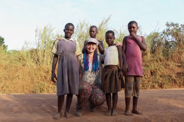 Kampala, Uganda - 17 Şubat 2015: Köyden Afrikalı fakir çocuklarla çevrili mavi örgülü genç bir Avrupalı kız.