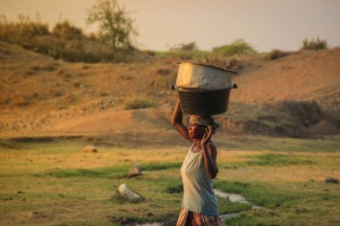 Kampala, Uganda - 17 Şubat 2015: Afrika köylü kadın savanada günbatımında kafasında bir havza su taşıyor.