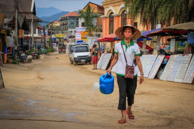 Vang Vieng, Laos - 1 Mart 2016: Elinde su kovası olan Asyalı bir kadın, Vang Vieng adlı küçük bir turist kasabasının caddesinde yürüyor..
