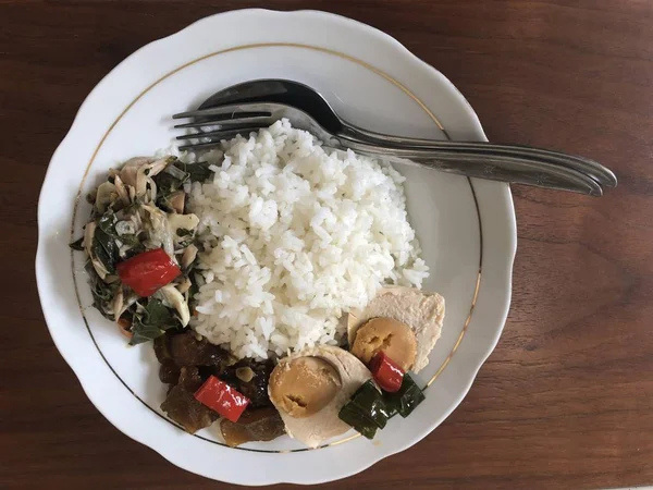 Rice with stewed vegetables and boiled eggs on plate with fork and spoon