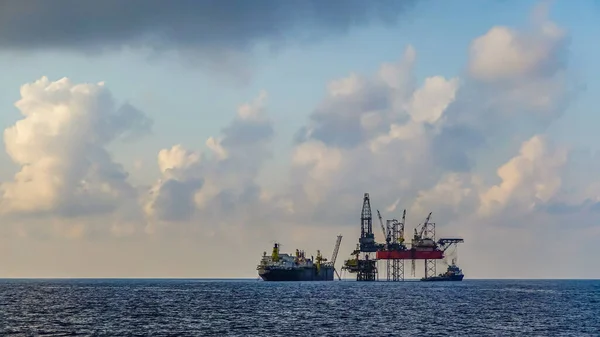 Drilling rig and floating production storage offshore ship in oil and gas offshore field with cloudy blue sky background
