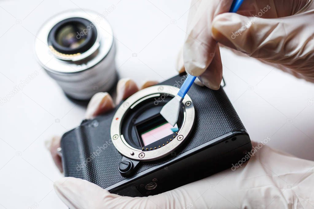 Close-up of mirrorless digital APS-C dirty camera matrix sensor cleaning and maintenance with swab, photographer cleaning photocamera on white background