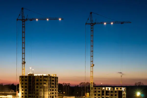 Tower cranes and unfinished multi-storey high near buildings under construction site in the sunset evening with dramatic colorful cloud background