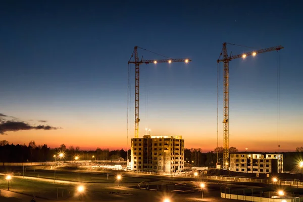 Tower cranes and unfinished multi-storey high near buildings under construction site in the sunset evening with dramatic colorful cloud background