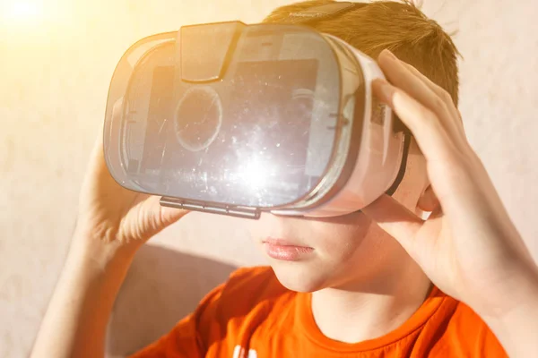 boy in orange t-shirt with VR AR 360 virtual reality glasses cardboard for mobile phone playing the game. Device for watching movies for travel and entertainment in 3d space.