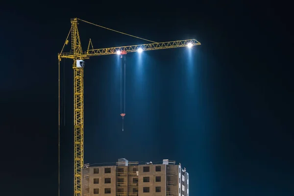 Tower cranes and unfinished multi-storey high near buildings under construction site in the night illuminates the searchlight