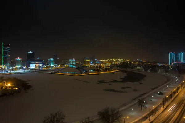 MINSK, BELARO - DICEMBRE 2018: luci della città di notte. Grattacielo luminoso riflesso nell'acqua del lago — Foto Stock