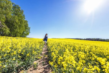 Yaz aylarında çiçek açan kolza tohumu sahada mavi elbiseli genç mutlu güzel kız. Beni kavramı takip