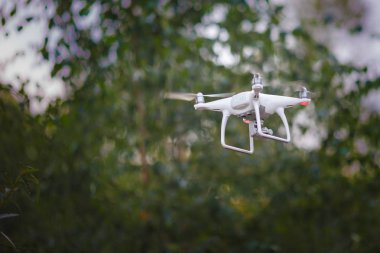 Kamera yeşil orman arka plan üzerinde beyaz uçan quadrocopter