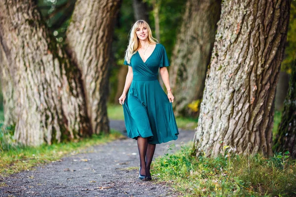 Yeşil uzun elbiseli sarışın bir kız bir meşe grove yürüyor — Stok fotoğraf