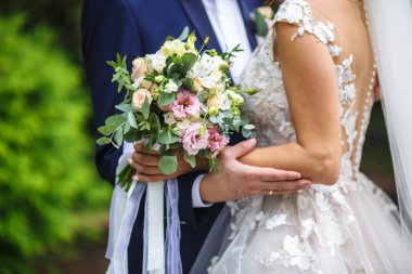 Gelin ellerini damadın omuzlarında koydu. pembe ve beyaz gül bir buket ile gelin sarılmak ve doğada damat öpmek. 