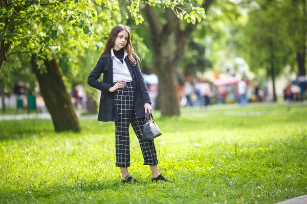 Portret małej pięknej stylowej dziewczynki z okularkami przeciwsłonecznymi i krótkimi spodniami w parku miejskim na zielonym tle lasu — Zdjęcie stockowe