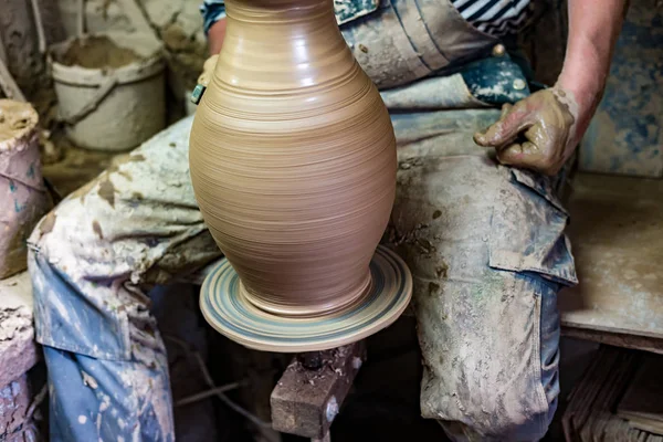 Craftsman in dirty clothes molding clay into desired shape on potter\'s wheel.