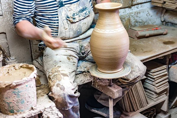Craftsman in dirty clothes molding clay into desired shape on potter\'s wheel.