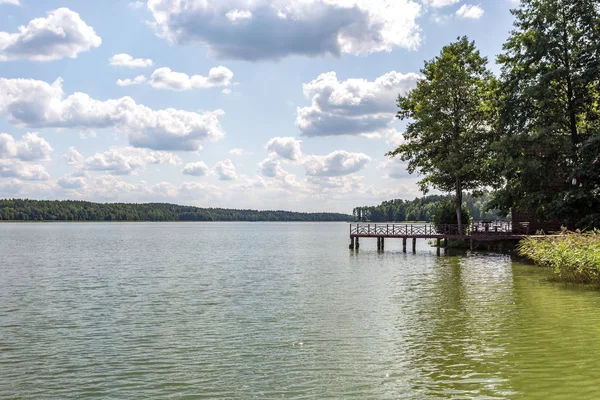 Muelle en la orilla de un gran lago en el día de verano con hermosas nubes. reflejo del cielo — Foto de Stock