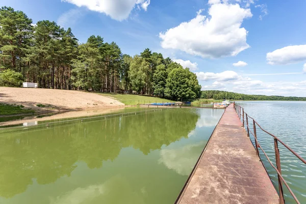 Muelle en la orilla de un gran lago en el día de verano con hermosas nubes. reflejo del cielo — Foto de Stock