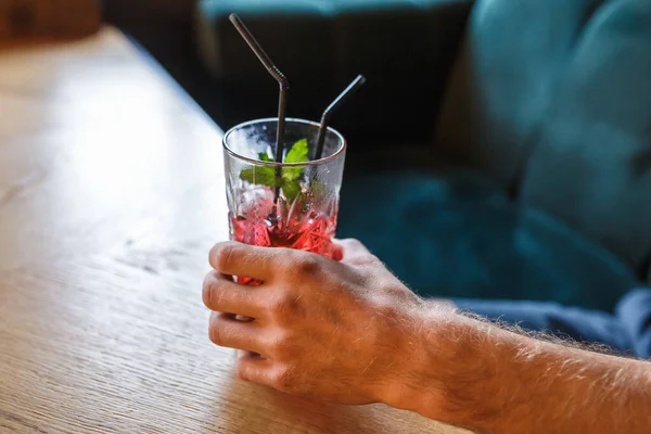 Koktail merah dalam gelas dengan mint dan dua tabung di tangan manusia dalam — Stok Foto