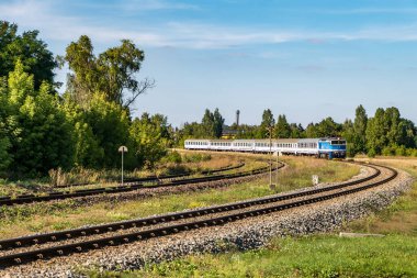 Yolcu treni güneşli bir günde tarlalar arasında yolculuk eder.