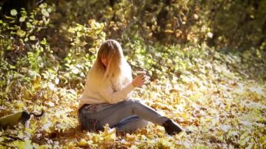 Kız sonbahar ormanında yerde oturuyor. 