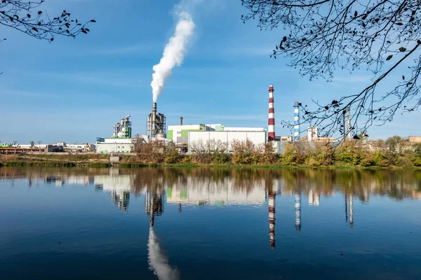 pipes of woodworking enterprise plant sawmill near river. Air pollution concept. Industrial landscape environmental pollution waste of thermal power plant