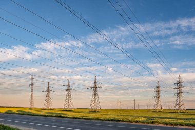Güzel akşam bulutlarının arkasındaki yüksek voltajlı elektrik kulelerinin silueti.