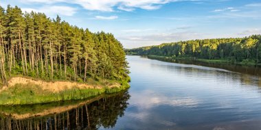 Güneşli bir günde, güzel, geniş bir nehir veya kanal manzarası. Mavi yansımalı, suda güzel bulutlar var.