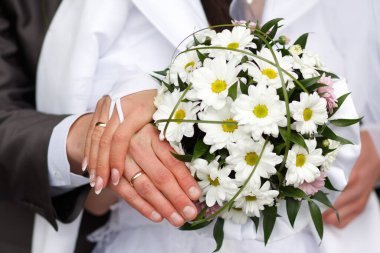 Damat gelini düğün buketiyle kucaklıyor. Yeni evli bir çiftin elindeki yüzükler. Gelin ellerini damadın omuzlarına koydu.. 