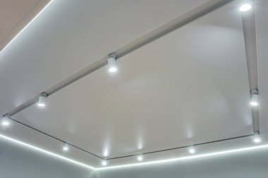 Halojen lambalı asma tavan ve boş bir oda ya da evde alçıpan inşaatı. Gergin tavan beyaz ve karmaşık şekil.