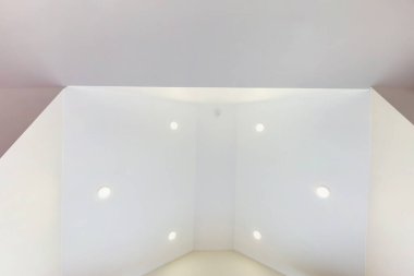 Halojen lambalı asma tavan ve boş bir oda ya da evde alçıpan inşaatı. Gergin tavan beyaz ve karmaşık şekil.