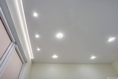 Halojen lambalı asma tavan ve boş bir oda ya da evde alçıpan inşaatı. Gergin tavan beyaz ve karmaşık şekil.