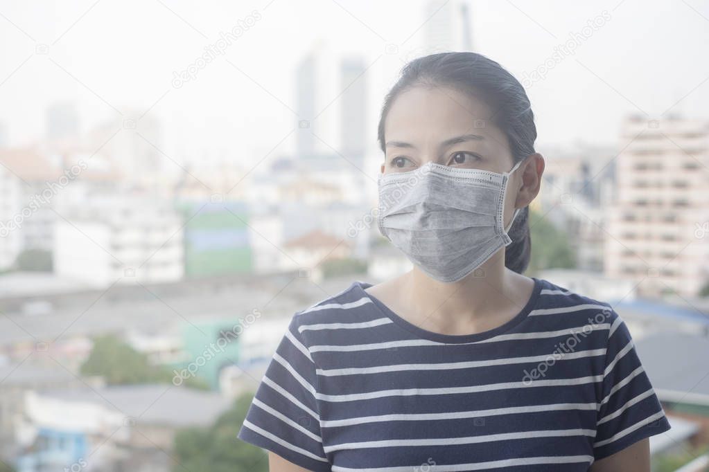 Woman wearing face mask of N95 because of air pollution in the city have particulate matters or PM 2.5 with city building background