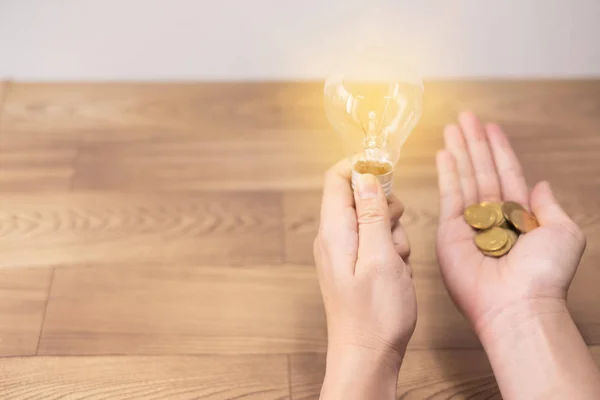 Concepto de nueva idea, las mujeres jóvenes mano sosteniendo bombilla y monedas en fondos de madera y nuevo concepto de idea ahorrar energía para salvar la tierra — Foto de Stock