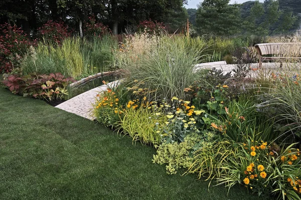 A garden with a water feature and selection of grasses and flowers